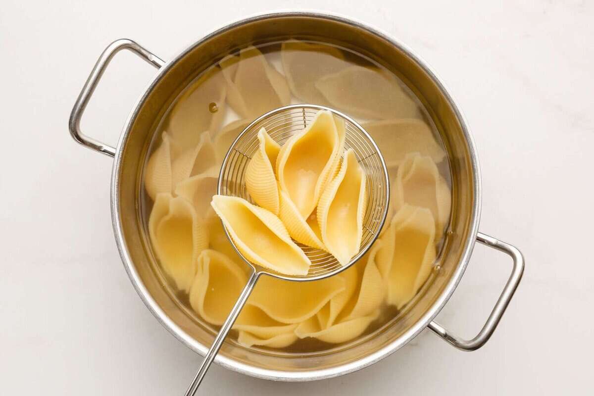 Lifting cooked pasta shells from pot of boiling water.