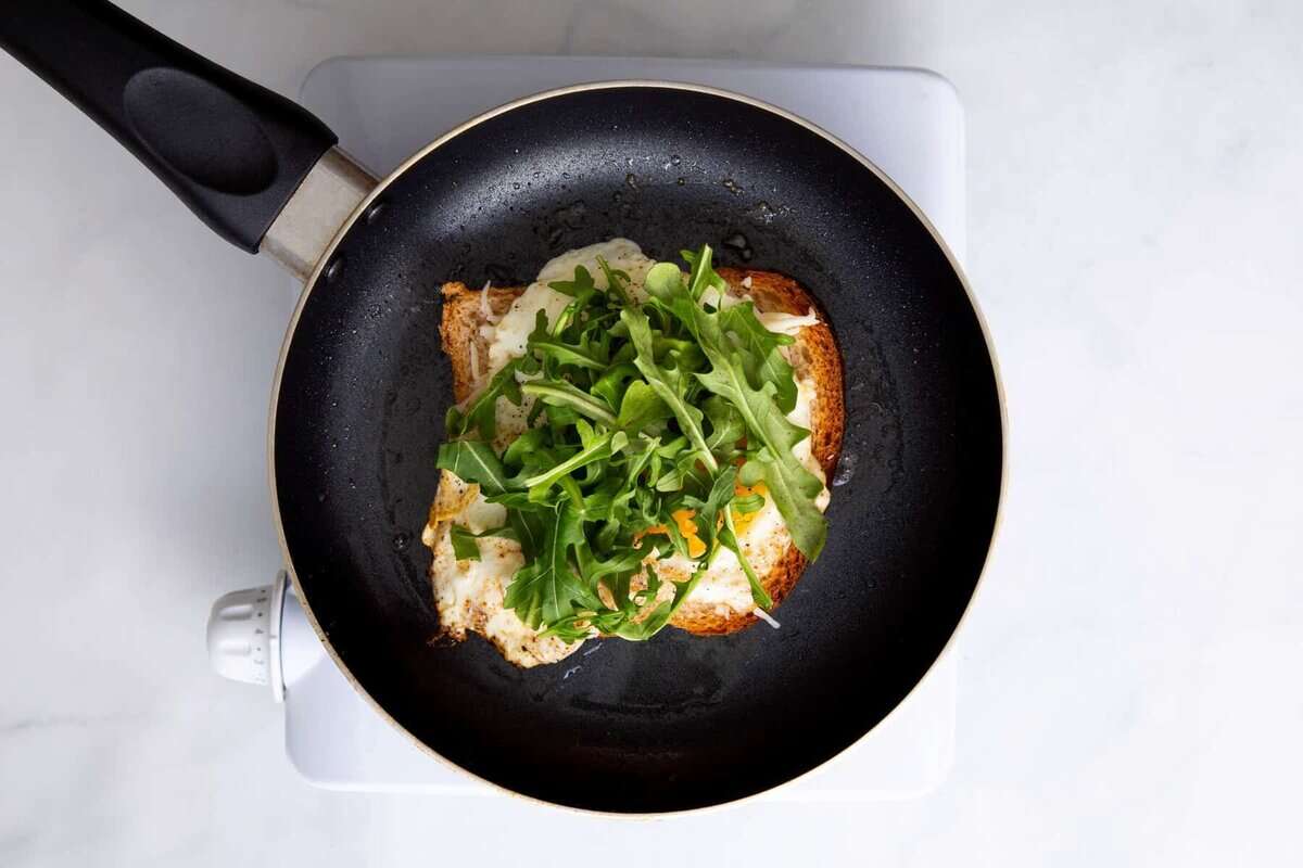 Arugula added to egg sandwich in pan.