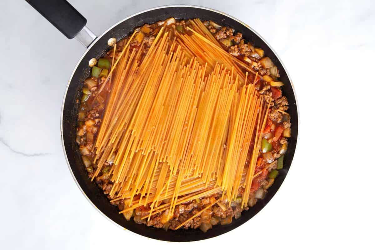 Dry spaghetti added to skillet with sauce for taco spaghetti.