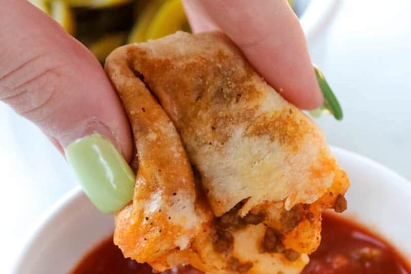 Hand dipping piece of taco stick into marinara sauce held in small white bowl