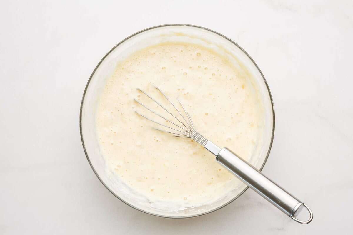 Banana pancake batter in bowl with whisk.