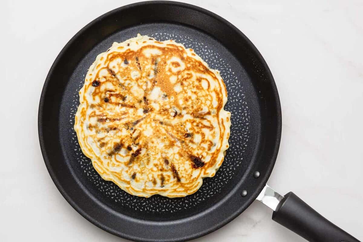 Chocolate chip pancake cooking in skillet.