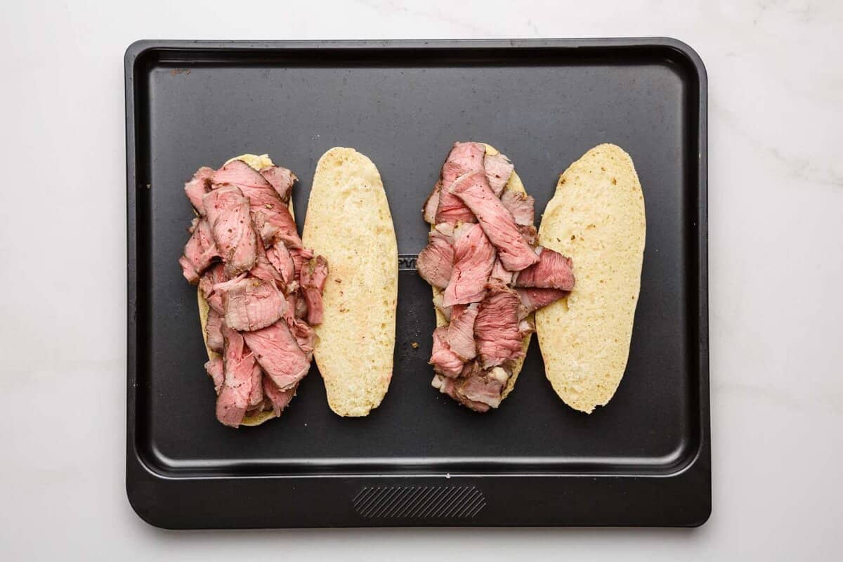 Sliced beef layered onto hoagie rolls.