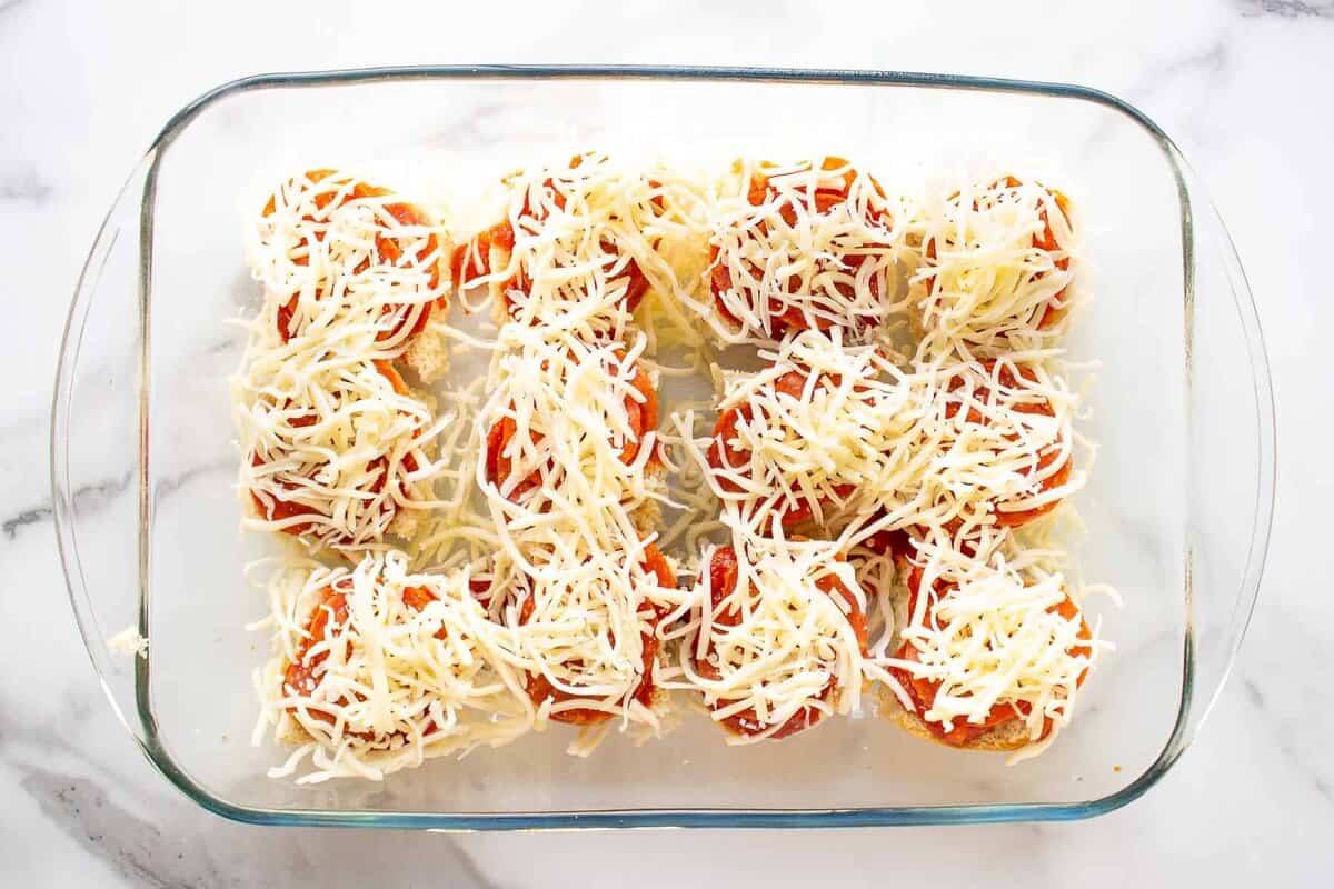 Shredded mozzarella layered onto pizza sliders.