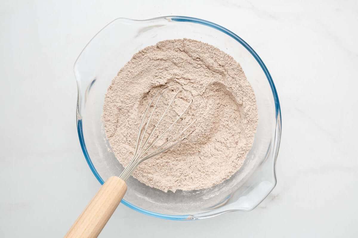 Mixing dry ingredients for wacky cake recipe in bowl with whisk.