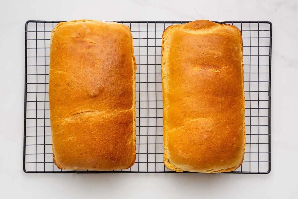 Two loaves of white sandwich bread on wire rack.