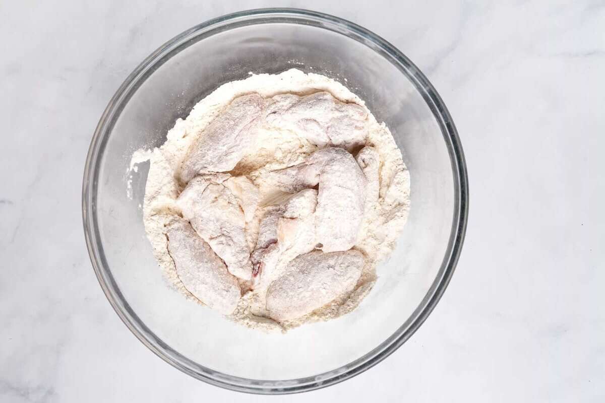 Chicken wings in bowl of flour and seasonings.