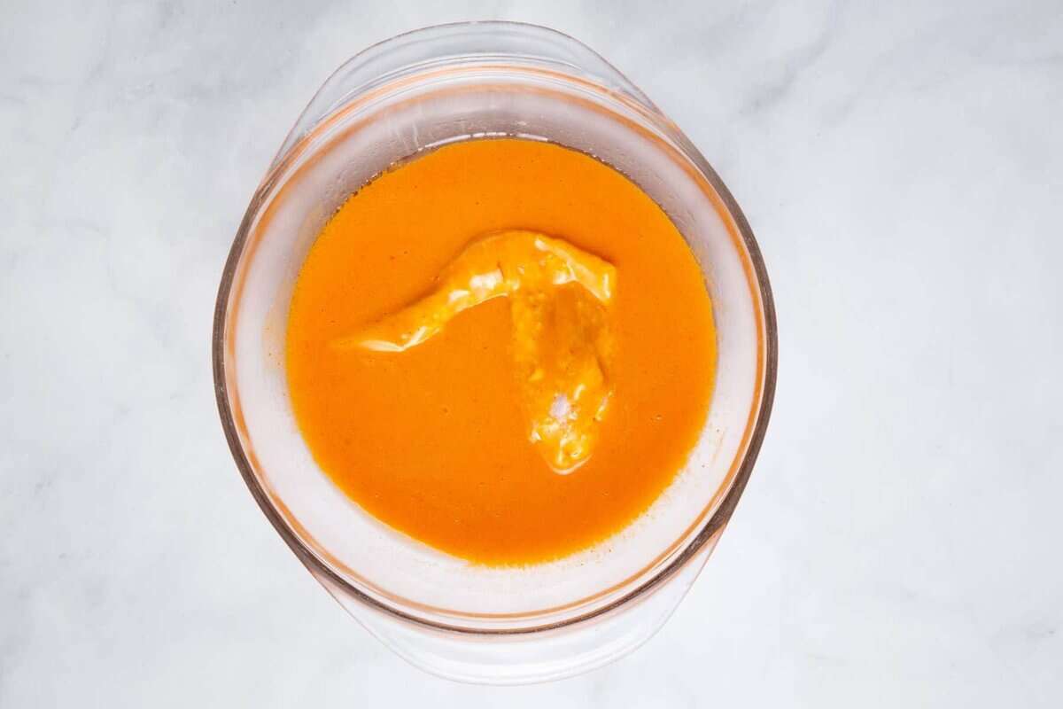 Chicken wing being dipped into buffalo sauce.