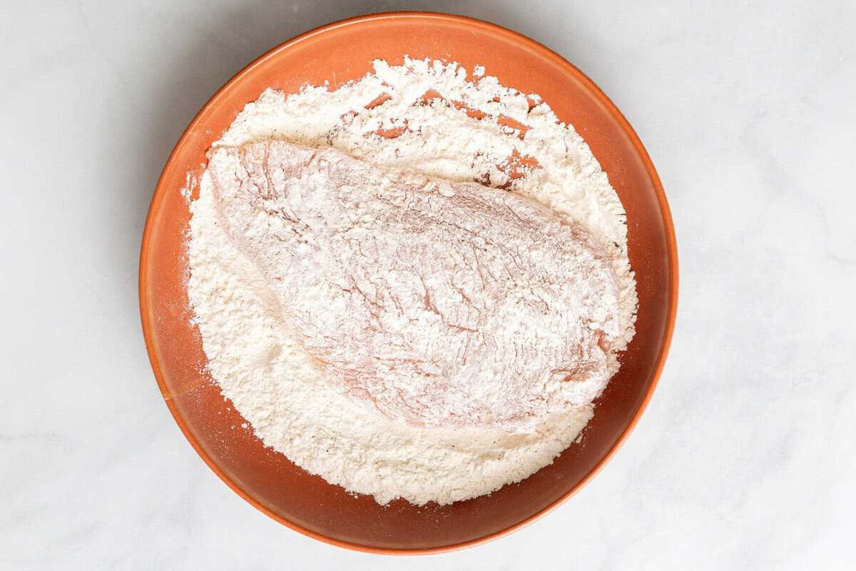 Chicken breast being dredged in flour.
