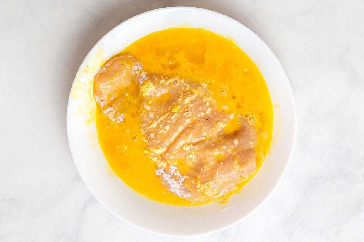 Chicken breast being dredged in egg.