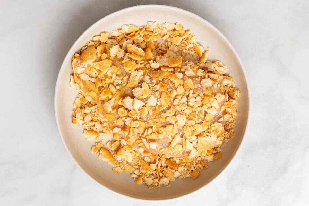 Chicken breast being dredged in Ritz crackers.