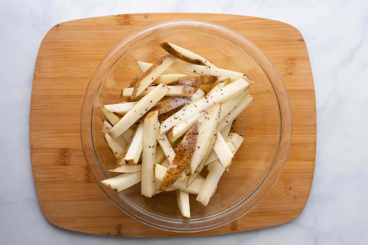 Seasoned uncooked French fries in bowl.