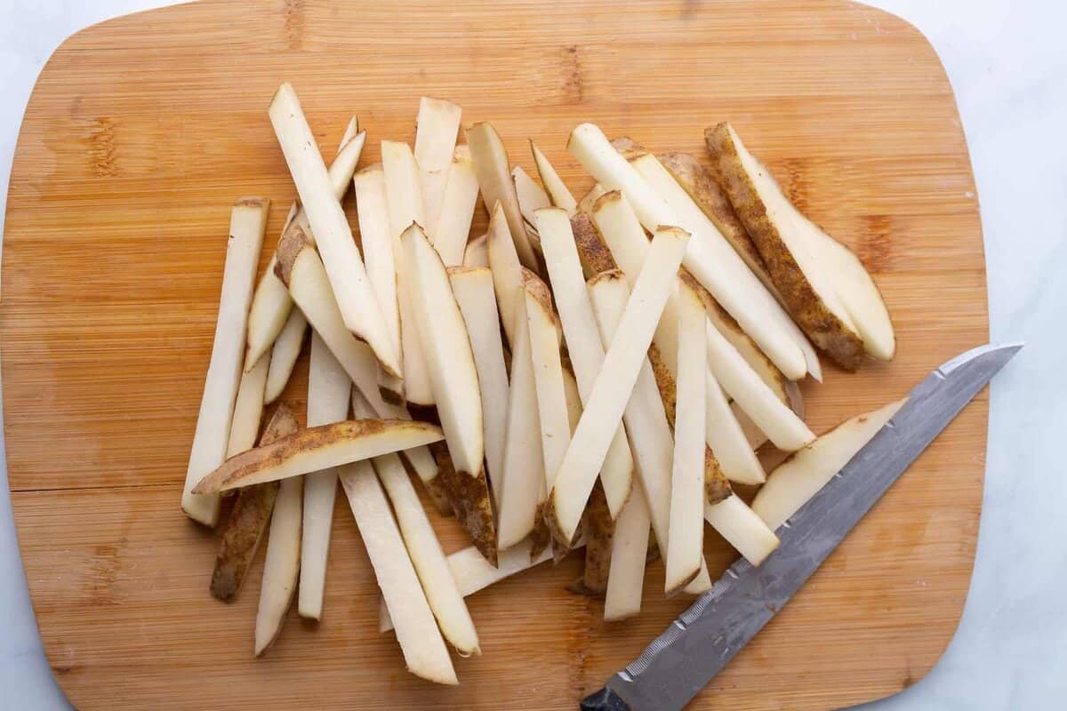 Potatoes cut into fries on cutting board.