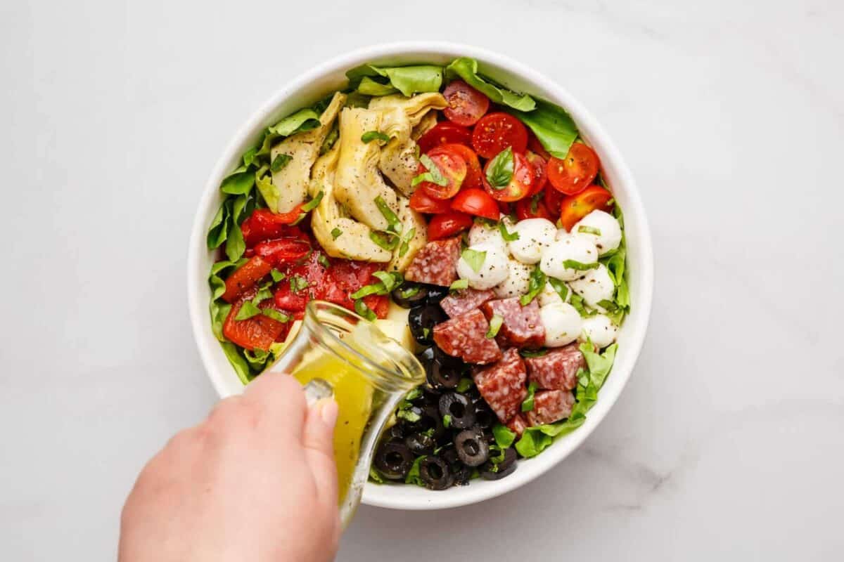 Pouring Italian dressing onto chopped antipasto salad.