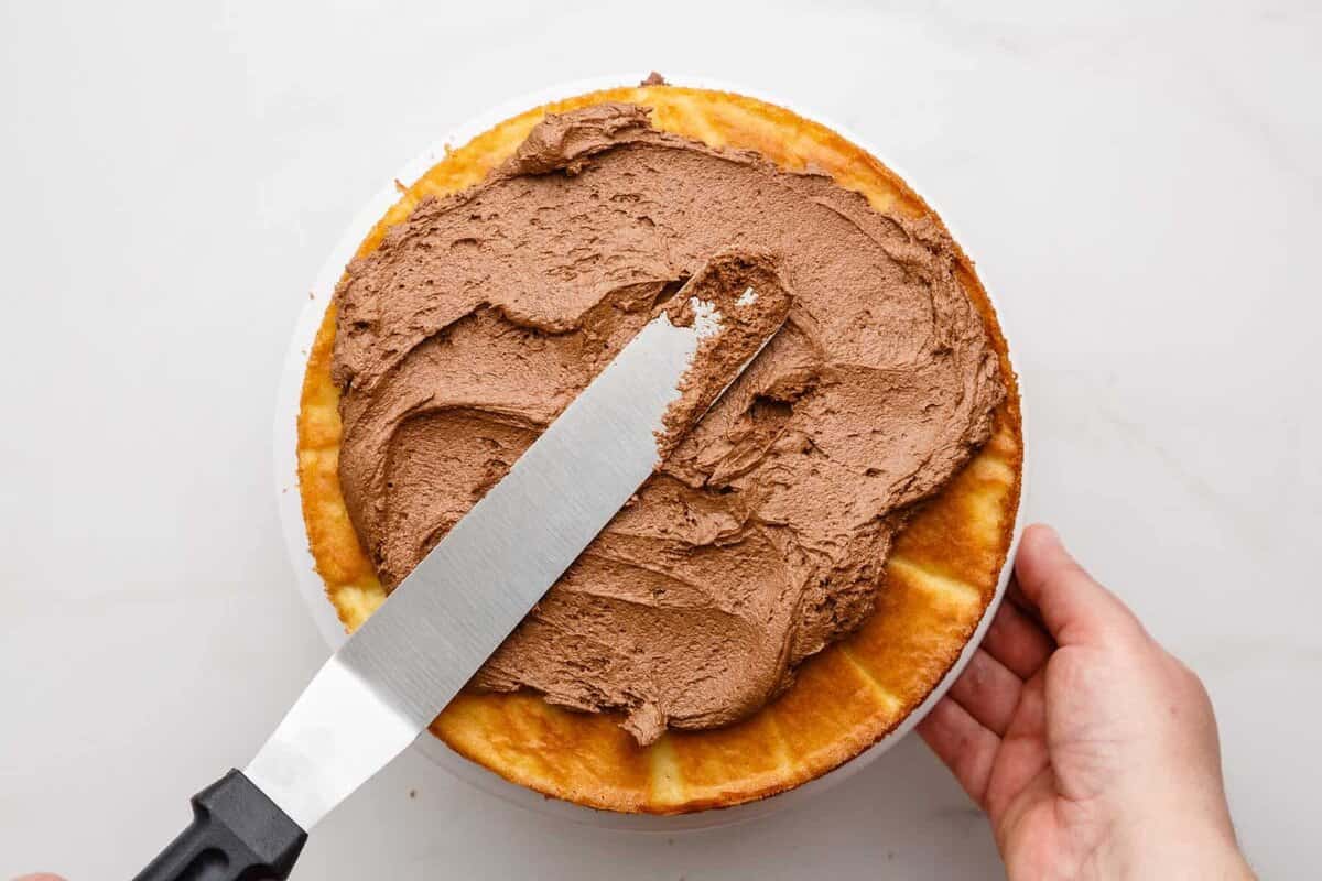 Spreading chocolate frosting on homemade birthday cake.