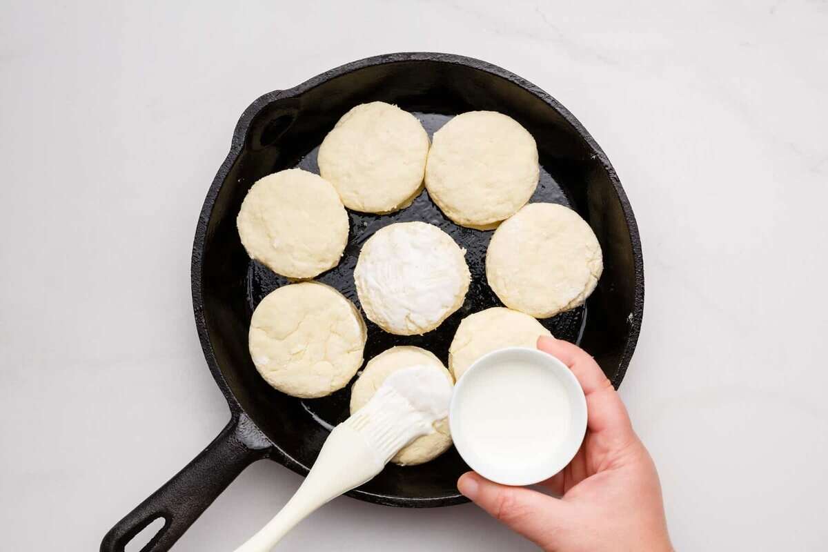 Brushing cream on buttermilk biscuits in skillet.