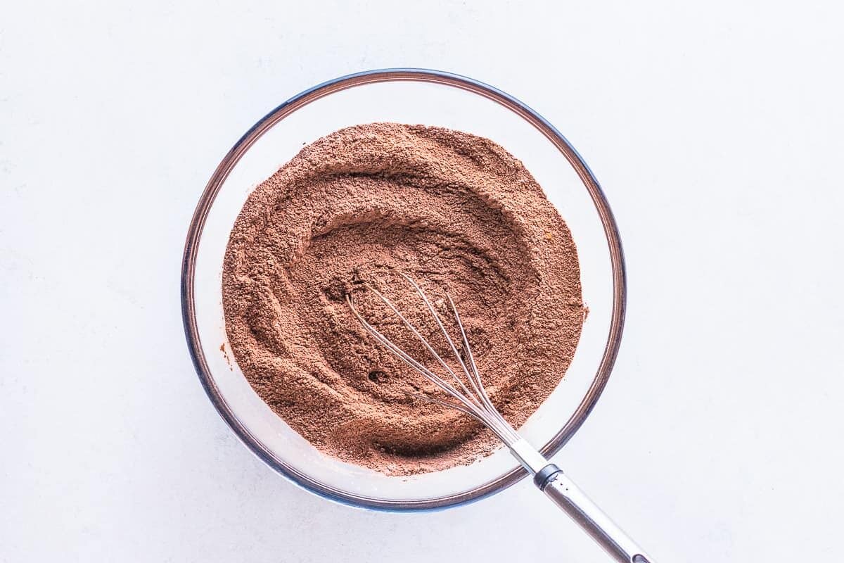 Dry ingredients for chocolate cake in bowl with whisk.