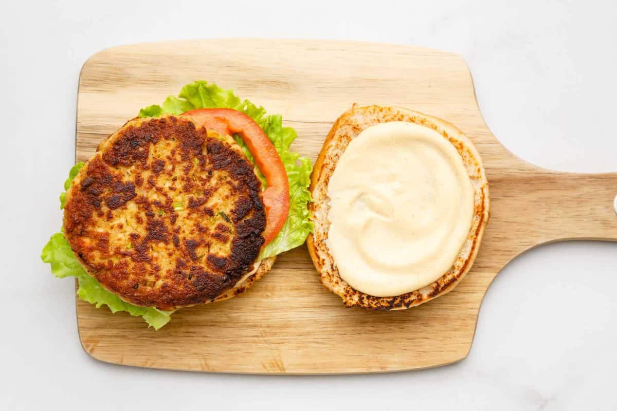Crab cake sandwich being assembled on cutting board.