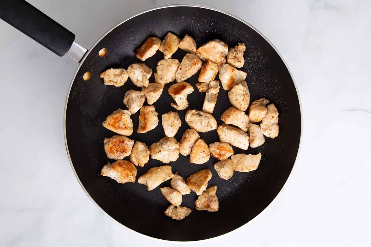 Chicken pieces cooking in skillet.