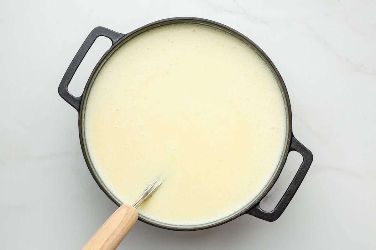 Cheesy potato soup in pot with whisk.