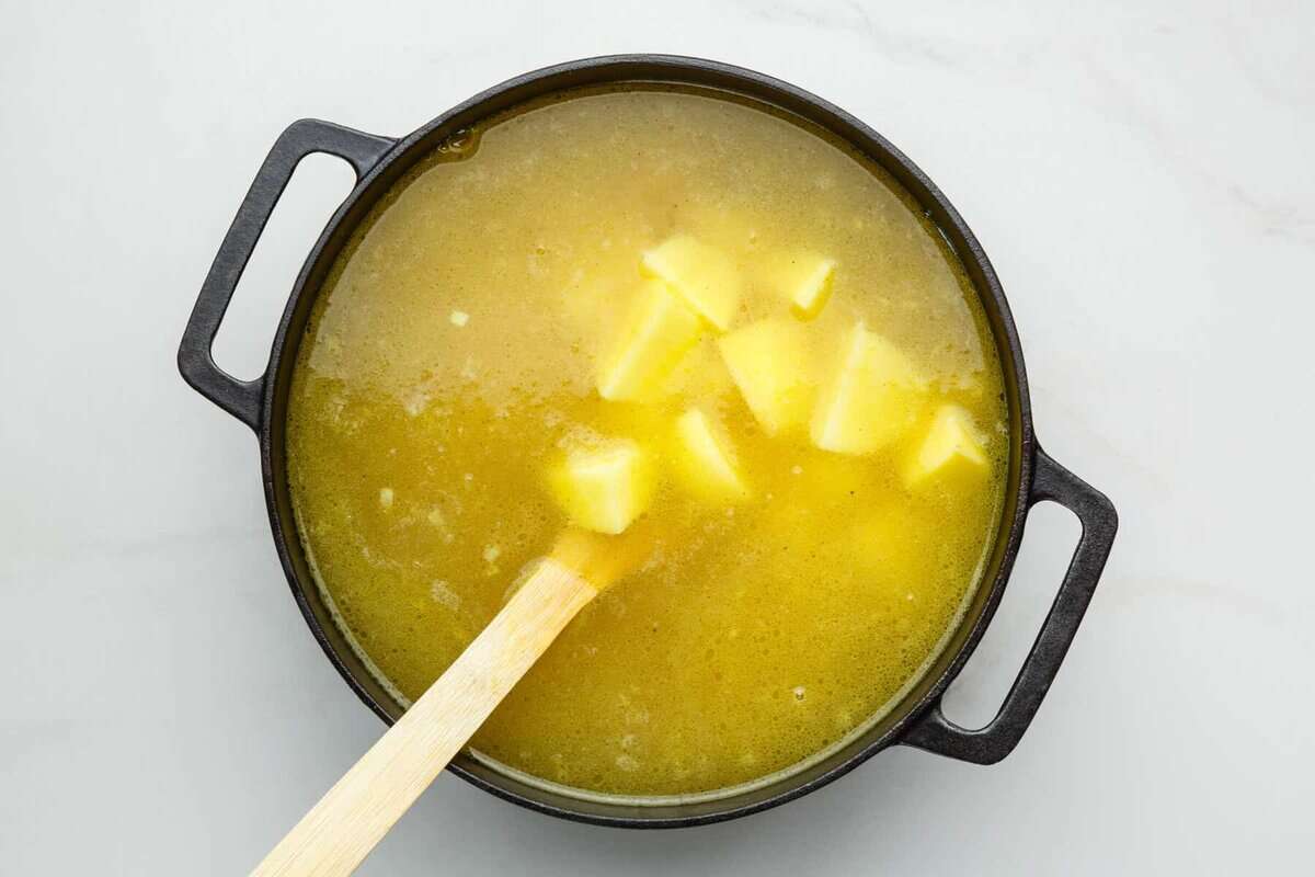Potatoes and broth in pot with wooden spoon.