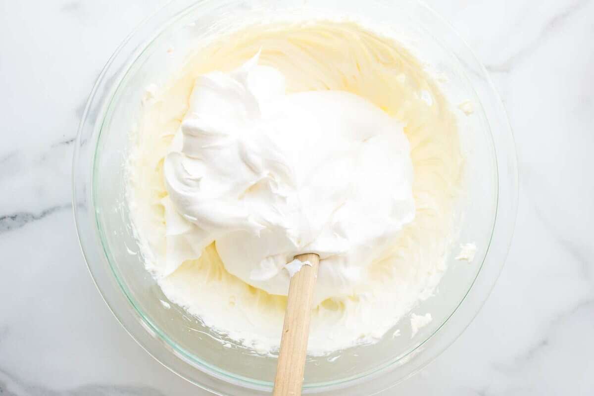 Folding cool whip into cream cheese mixture in bowl.