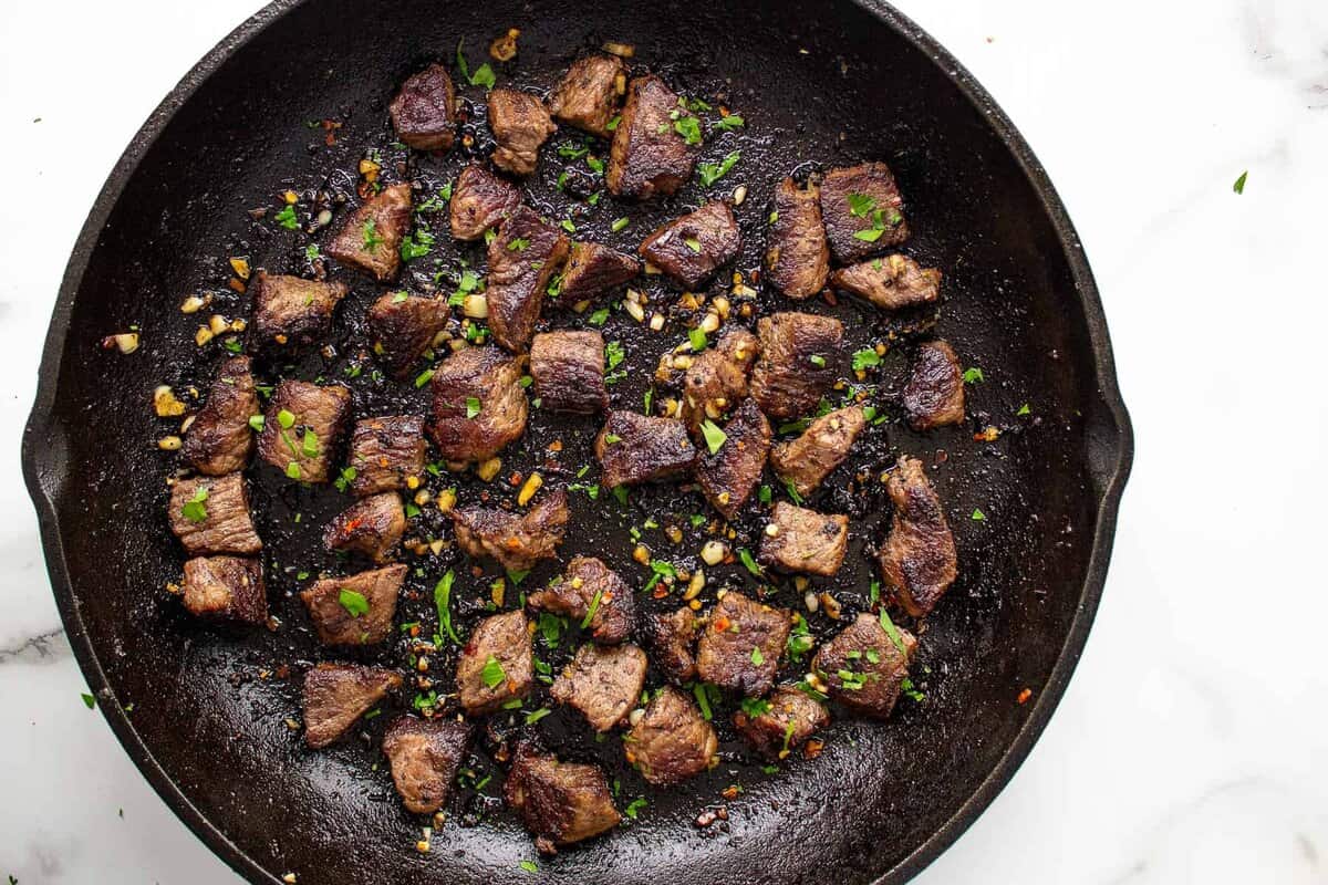 Steak bites with garlic butter in skillet.