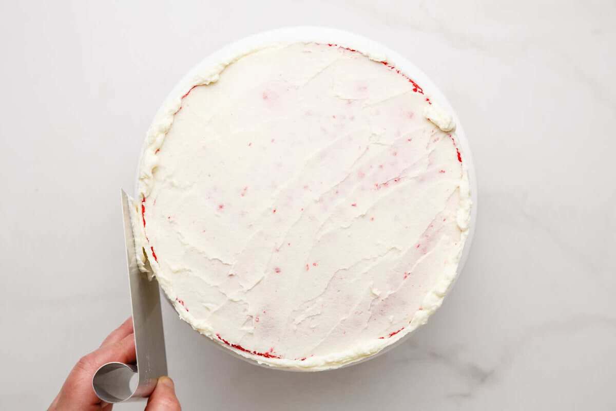Crumb coat being applied to rainbow layer cake.