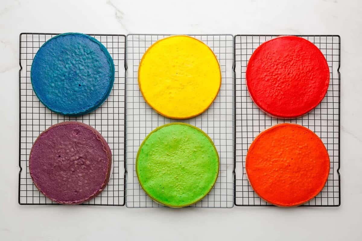 6 colorful cake layers on wire racks.