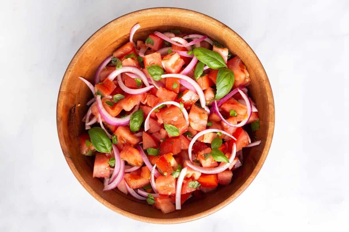 Tomato salad with onions and basil in wood bowl.