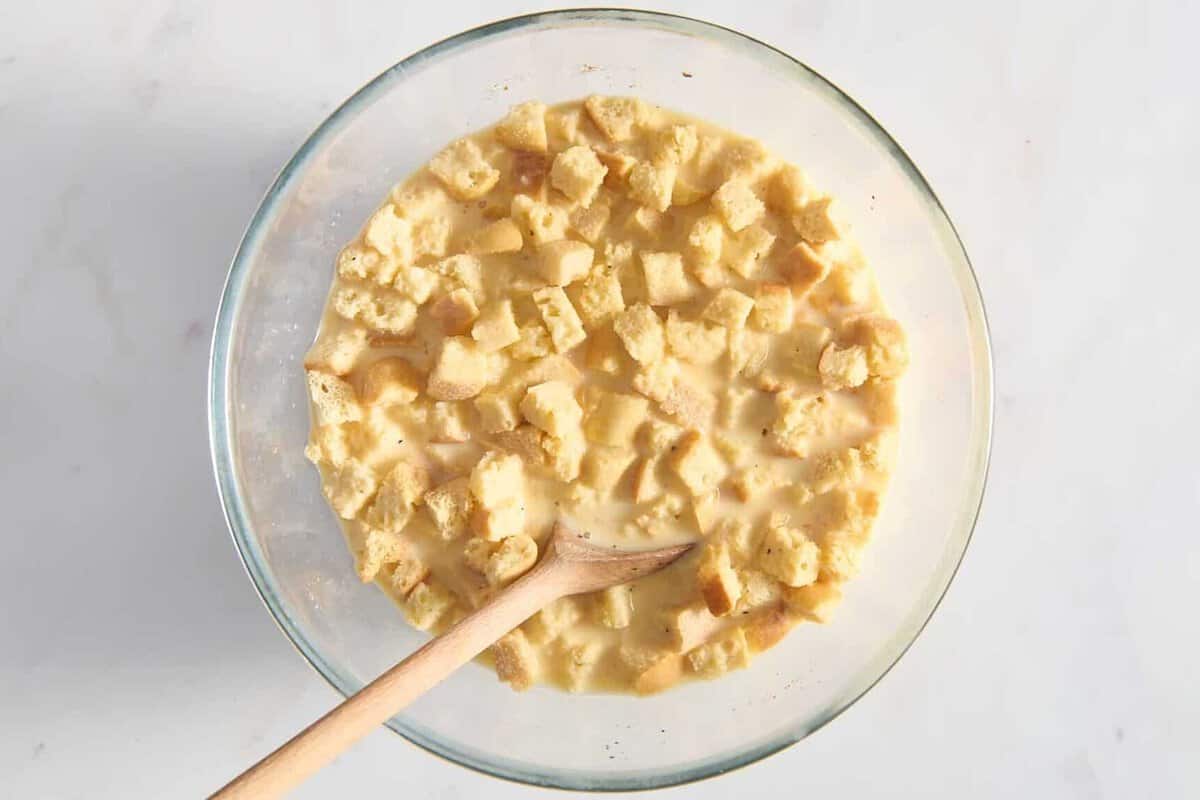 Egg and bread mixture in bowl with wooden spoon.