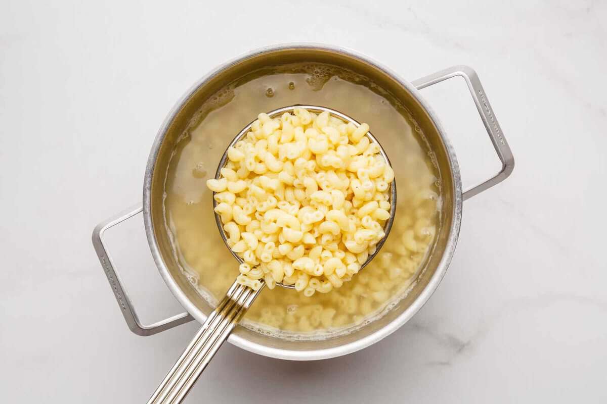 Slotted spoon lifting macaroni from pot.