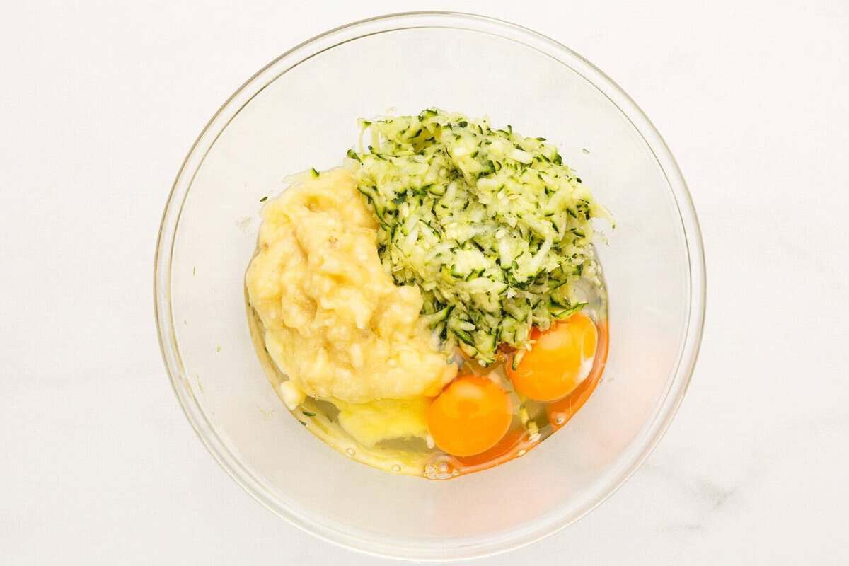 Eggs, mashed banana, oil, and zucchini in glass bowl.