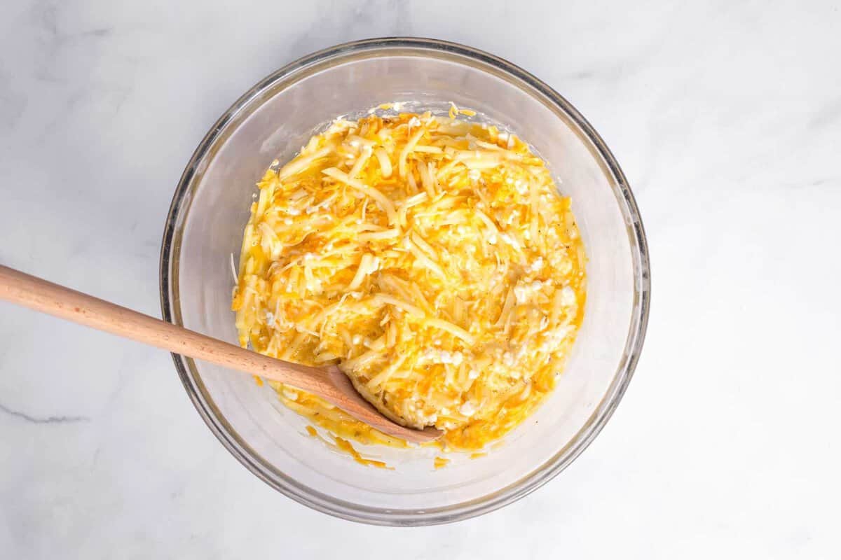 Eggs and cheese in glass bowl with wooden spoon.