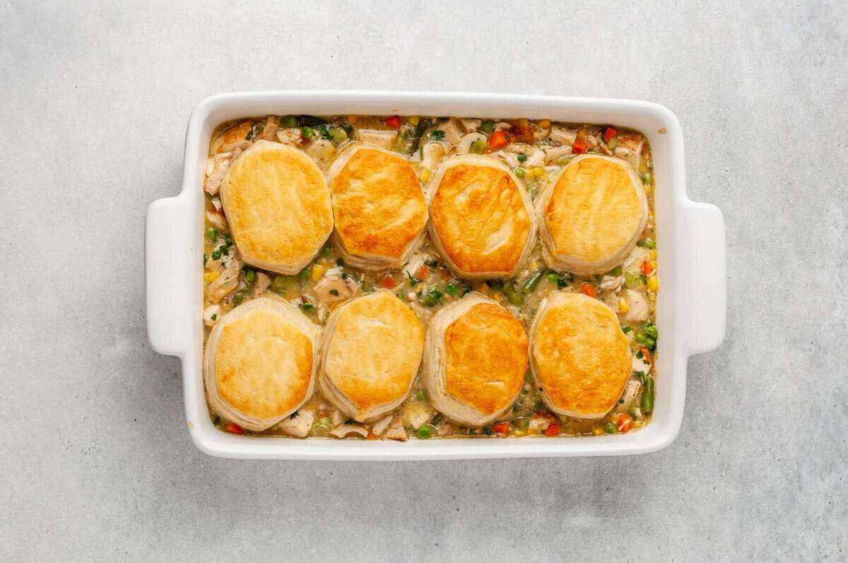 Chicken pot pie casserole topped with biscuits in baking dish.