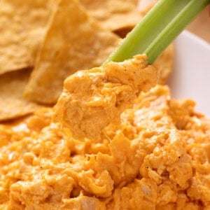 Buffalo chicken dip in a white bowl with celery sticks and tortilla chips
