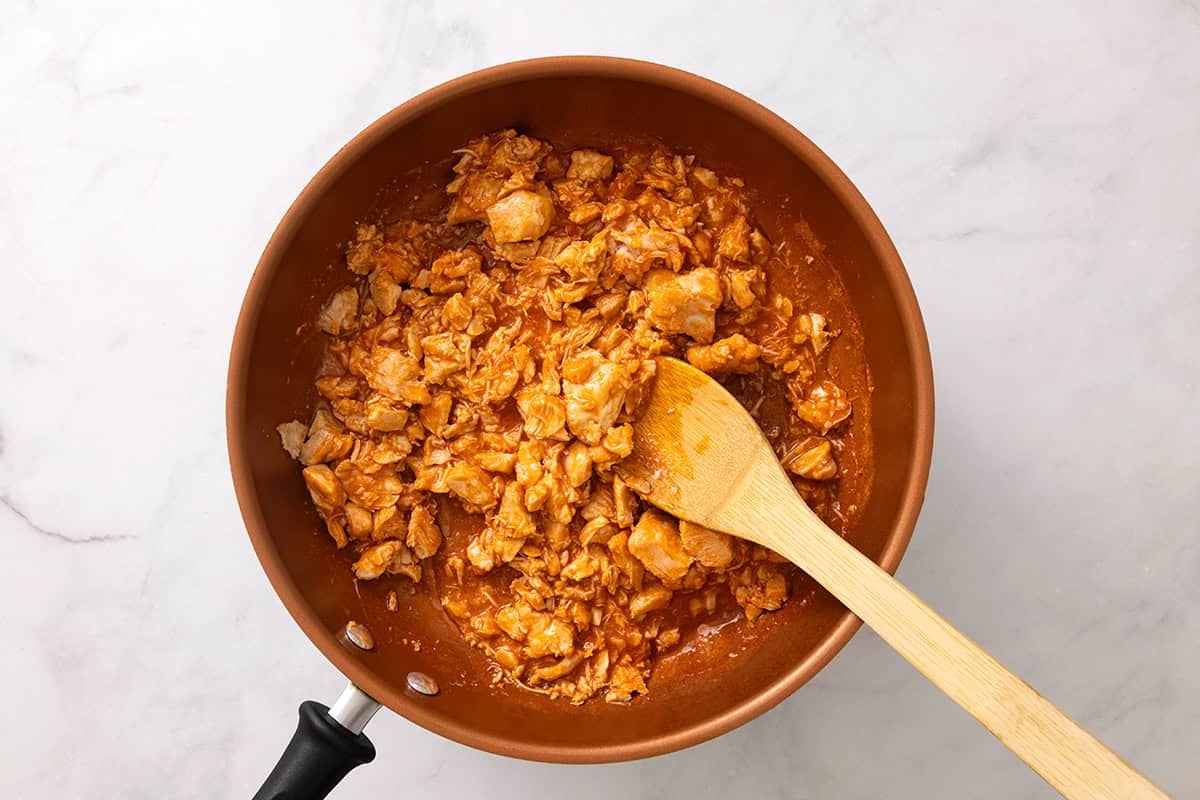 Shredded chicken and buffalo wing sauce warming in a skillet.