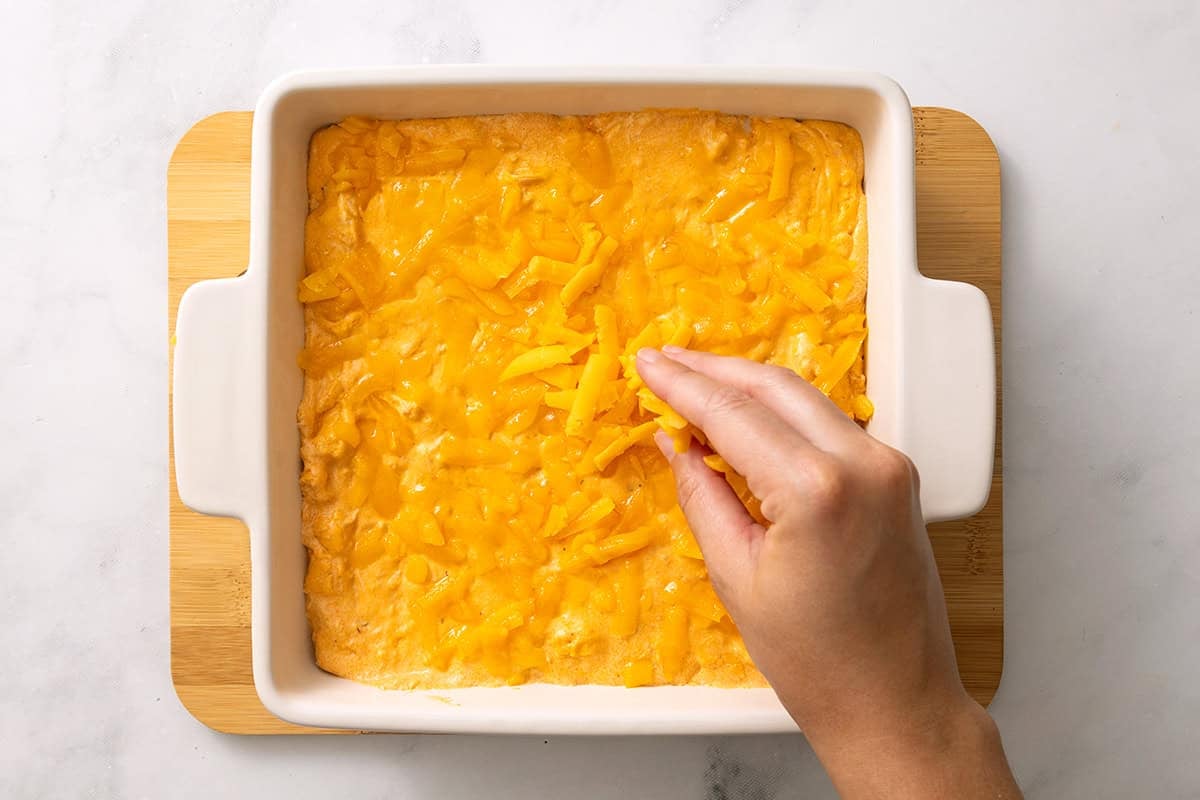Shredded cheddar sprinkled over buffalo chicken dip before baking.