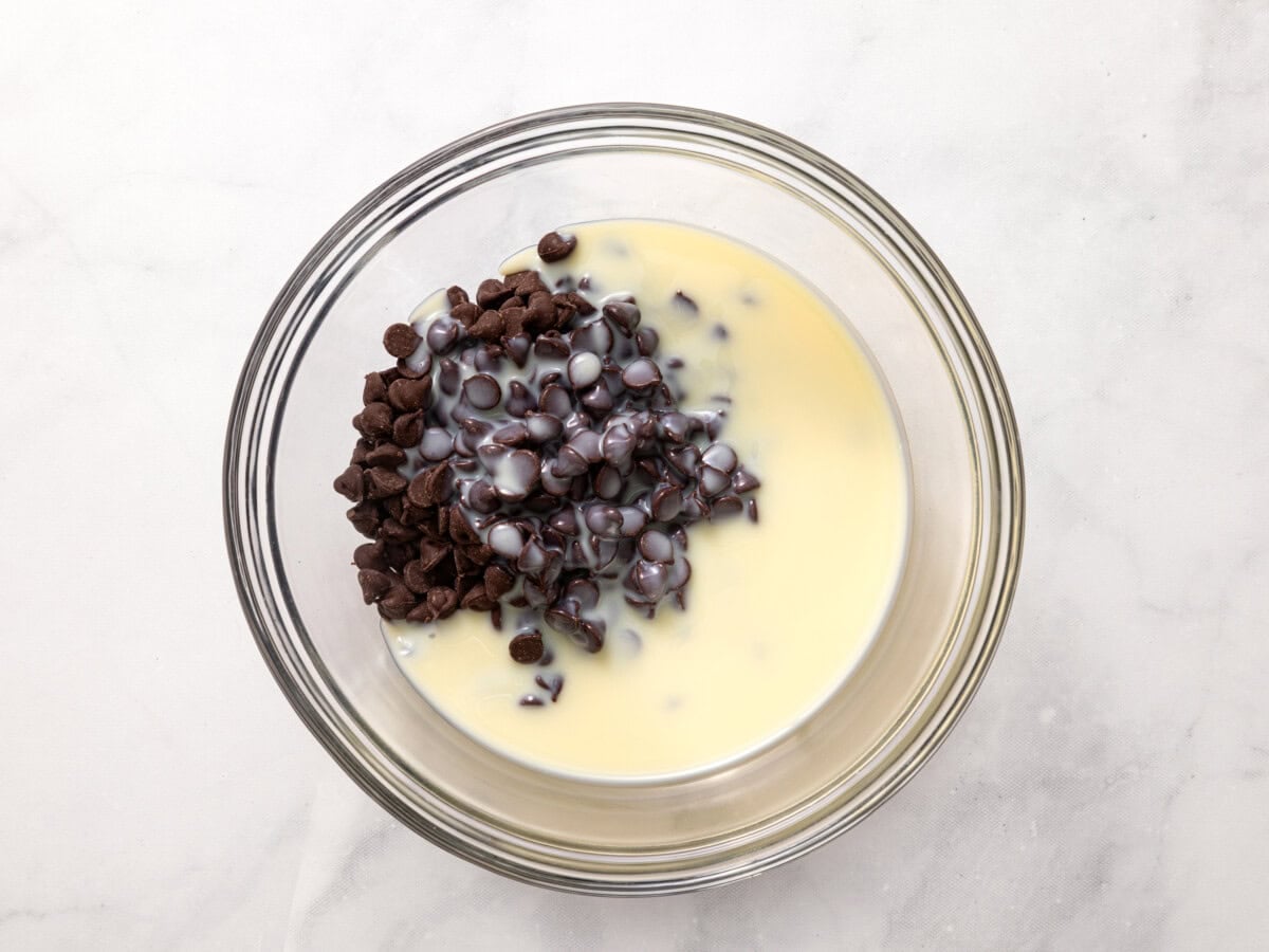 Condensed milk and chocolate chips in glass bowl.
